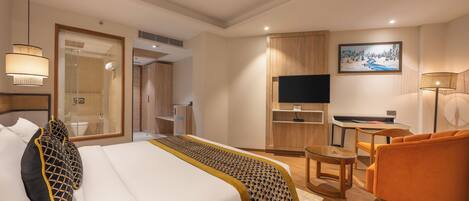 A hotel room with a bed, a desk, a chair, a TV, and a painting on the wall.