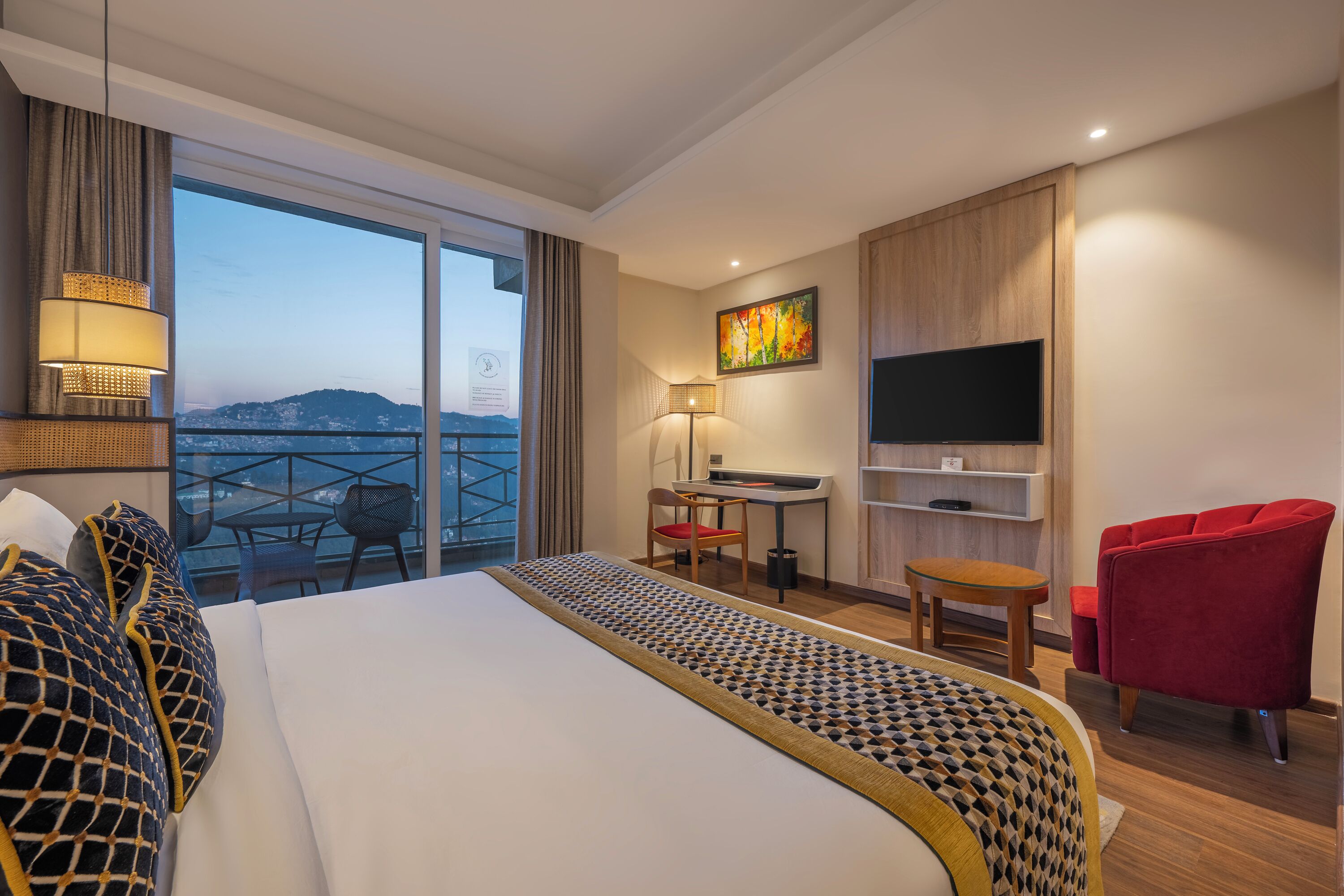 Een hotelkamer met een bed, een bureau, een stoel, een televisie en een balkon met uitzicht.