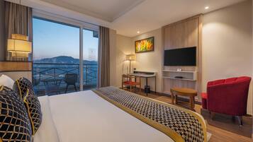 Een hotelkamer met een bed, een bureau, een stoel, een televisie en een balkon met uitzicht.
