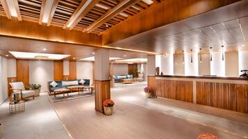 A spacious lobby with wooden paneling, a reception desk, seating areas, and potted plants.