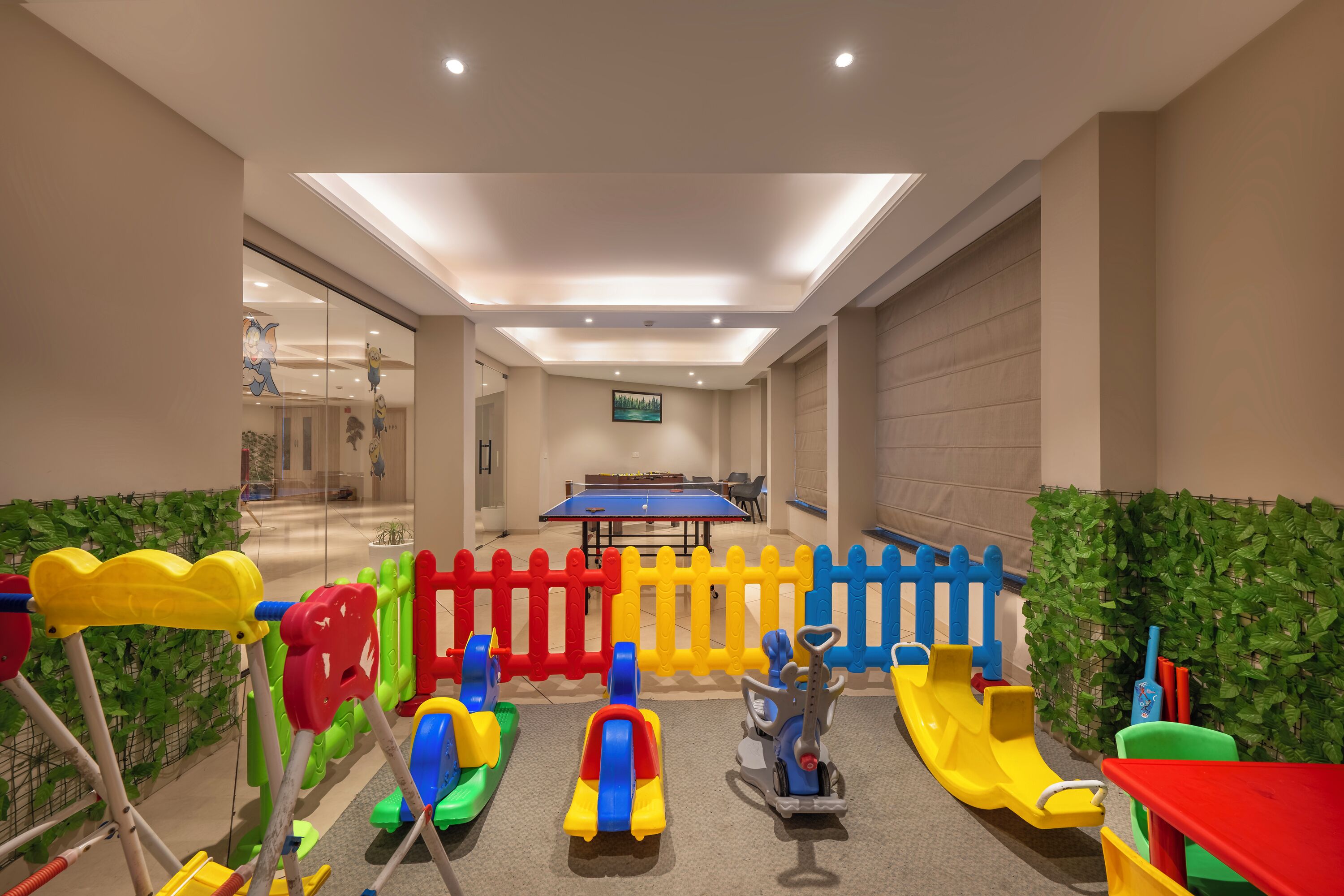 Un espace de jeux pour enfants avec des équipements colorés, une table de ping-pong et un mur végétal.