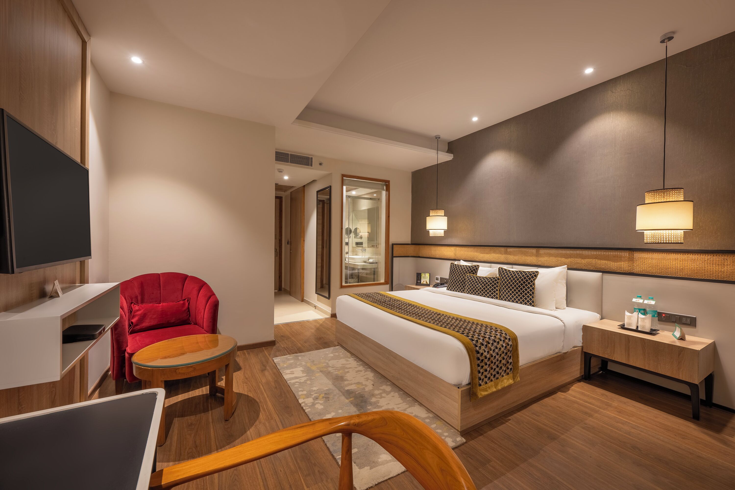 Une chambre d’hôtel moderne avec un lit, un fauteuil rouge, une petite table, une table de chevet avec une lampe et un téléviseur.