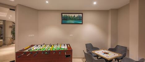 A room with a foosball table, a dining table with chairs, and a painting on the wall.