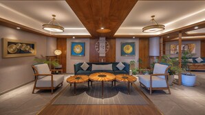 Una sala de estar moderna con techo de madera, un sofá central, dos sillones y tres mesas redondas de madera.
