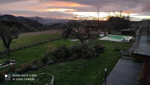 Ein Garten mit einer Holzterrasse, einem kleinen Pool und Blick auf ferne Hügel.