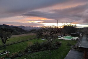Ein Garten mit einer Holzterrasse, einem kleinen Pool und Blick auf ferne Hügel.