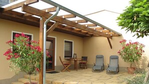 A covered patio with a wooden pergola, a small table with chairs, and potted plants. - Directly on the water with its own jetty in Berlin - Köpenick (Berlin)