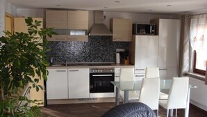 A modern kitchen with white cabinets, a black tiled backsplash, a built-in oven, and a dining area with a glass table and white chairs. - Directly on the water with its own jetty in Berlin - Köpenick (Berlin)