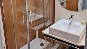A bathroom with a glass-enclosed shower, a white sink, a mirror, and a small stool. - Graça Terrace (Lisboa)