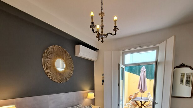 A bedroom with a large bed, bedside lamps, a wall-mounted air conditioner, and a chandelier. - Graça Terrace (Lisboa)