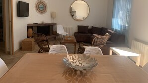 A modern living room with a wooden dining table, wicker chairs, a sofa, and a fireplace. - 4-star waterfront villa with exceptional sea views (Sari Solenzara)
