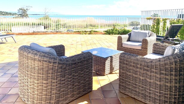 An outdoor patio with wicker furniture, a table, and an umbrella. - 4-star waterfront villa with exceptional sea views (Sari Solenzara)