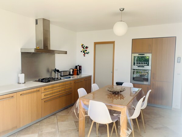 Una cocina moderna con armarios de madera, una campana extractora de acero inoxidable y un comedor con mesa de madera y sillas blancas.