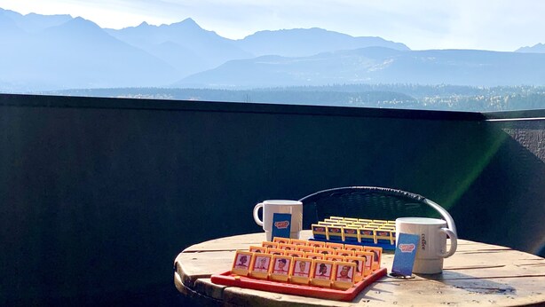 Ein Tisch mit Kaffeetassen und Streichholzschachteln auf einem Balkon mit Blick auf Berge.