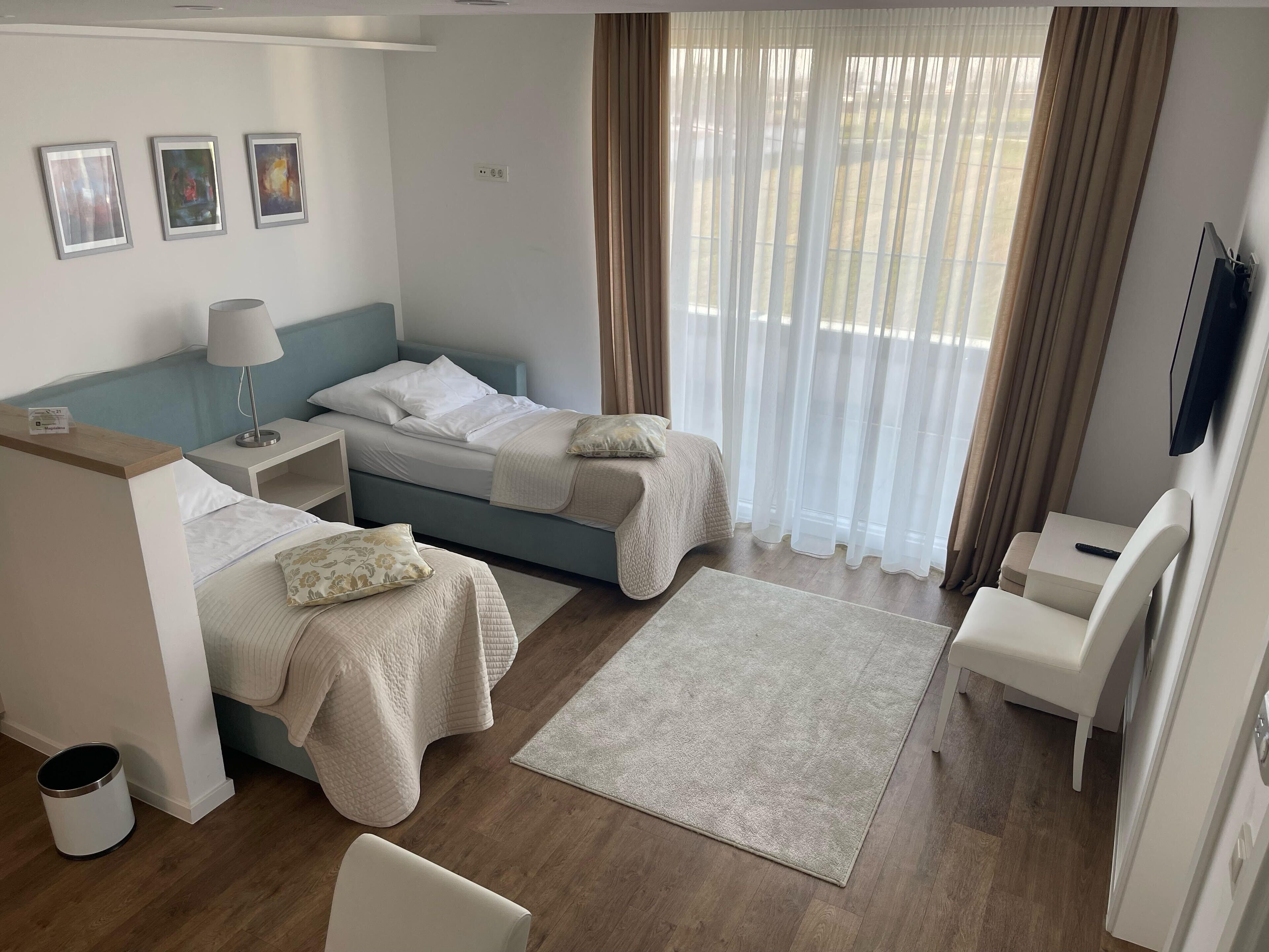 A hotel room with two beds, a desk, a chair, a TV, and a window with curtains.