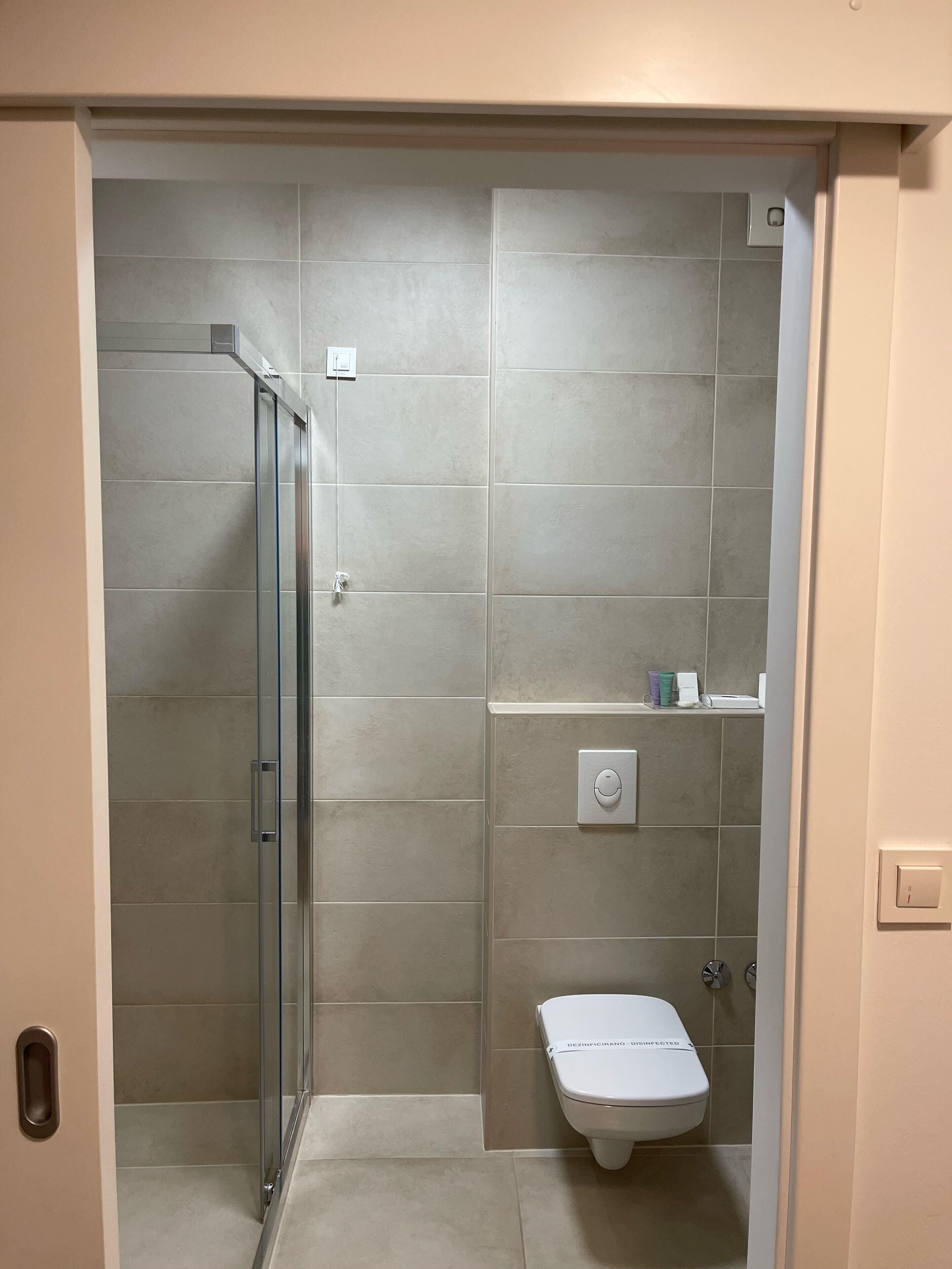 Een moderne badkamer met een douchecabine van glas, een toilet en een klein plankje met toiletartikelen.