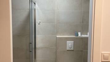 Een moderne badkamer met een douchecabine van glas, een toilet en een klein plankje met toiletartikelen.