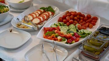 A buffet table with various dishes including sliced tomatoes, cucumbers, and olives.