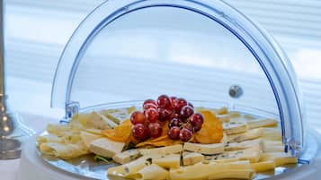 Eine Speisenauslage mit Pasta, Käse, Trauben und Chips unter einer Glaskuppel.