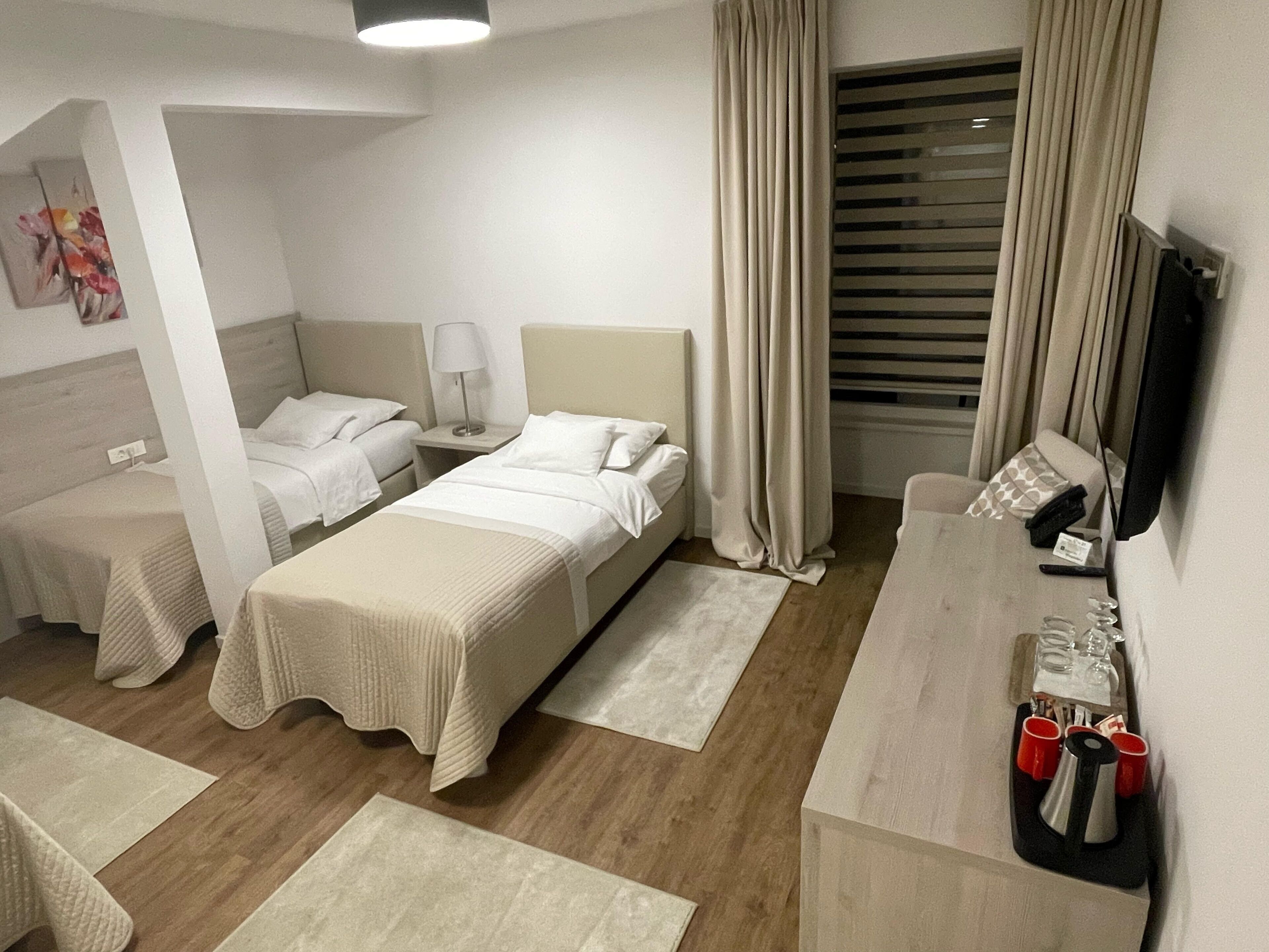 Une chambre d’hôtel avec deux lits simples, un bureau doté d’un téléviseur à écran plat, une petite table avec un téléphone et des verres, et une fenêtre avec des stores.