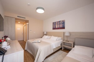 Una habitación de hotel con cama, mesitas de noche, un escritorio con teléfono y un cuadro en la pared.