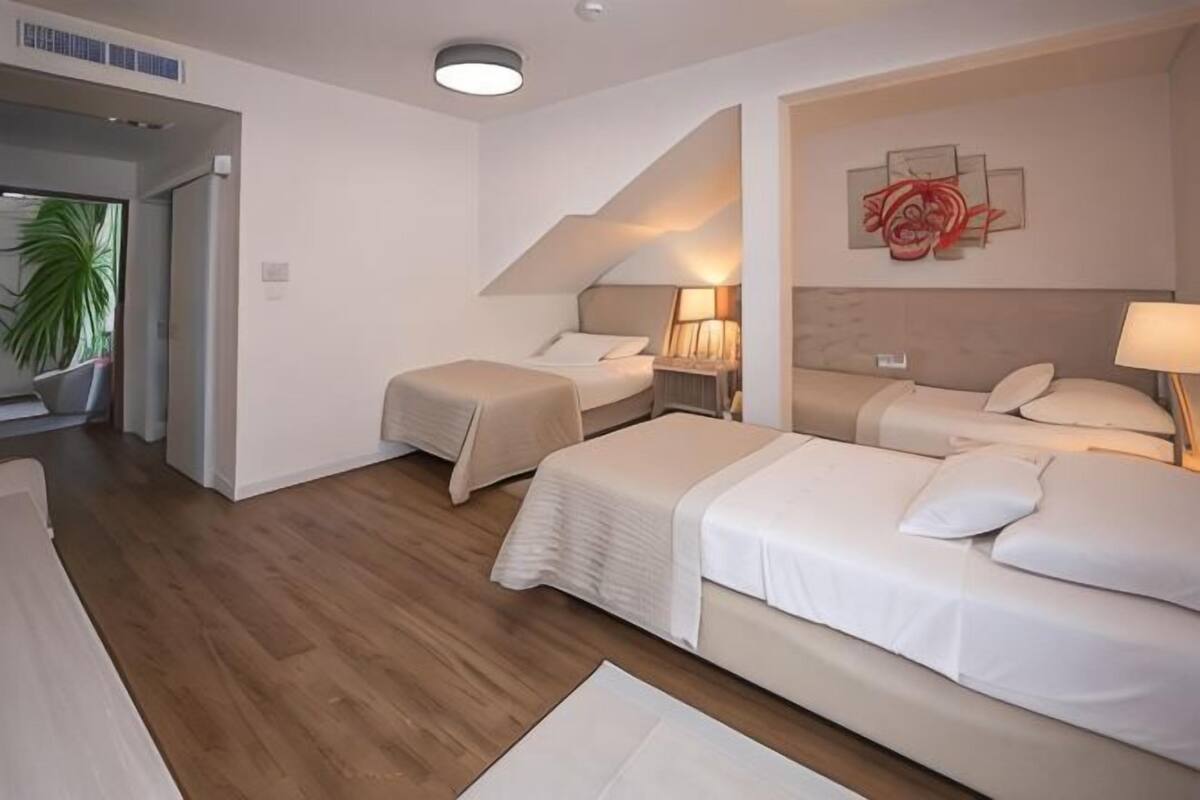 A hotel room with a wooden floor, two beds, a staircase, and a painting on the wall.