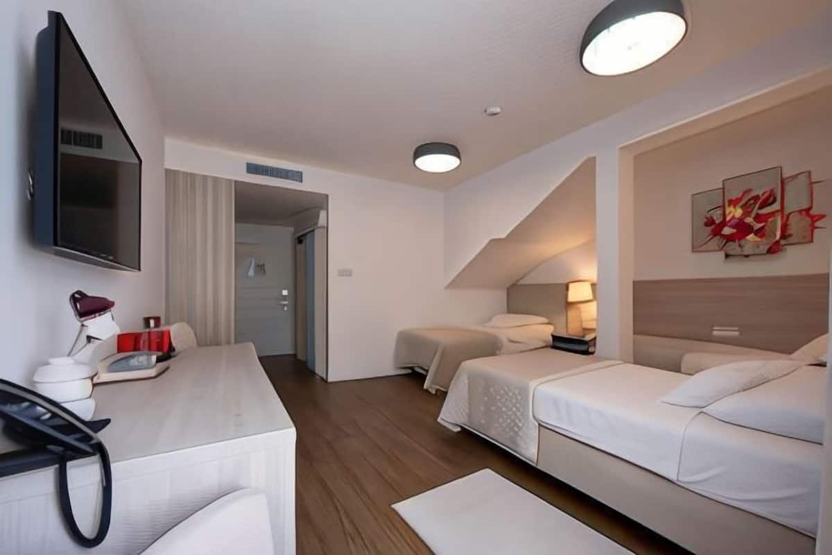 A hotel room with a desk, two beds, a TV, and artwork on the wall.