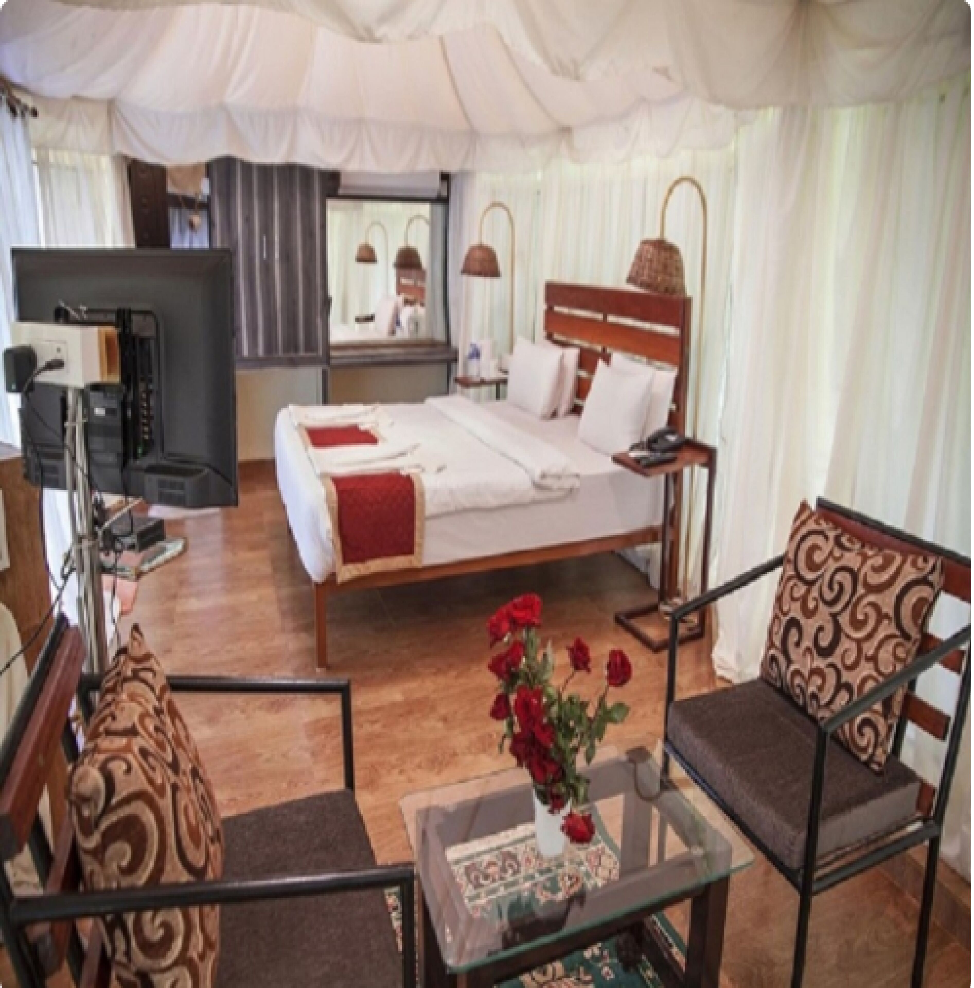 A hotel room with a bed, a chair, a table with a vase of flowers, and a television.