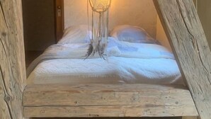 Ein Schlafzimmer im Loft-Stil mit schrägem Dach, einem hängenden Traumfänger und einem Bett mit weißer Bettwäsche.