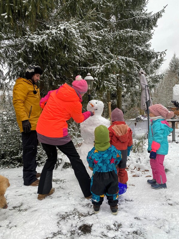 A group of people in a snowy outdoor setting, possibly a park or a natural area, with snow-covered trees and a snowman. - Charming holiday home in the Thuringian Forest, for 8 to 12 people (Gräfenthal)