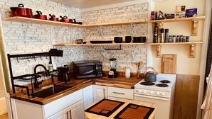 A compact kitchen with white cabinets, a wooden countertop, a stove, a microwave, and a coffee maker. - Waikiki Living, 4 blocks from surf, mountain views, king size bed and office! (Honolulu)