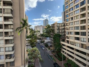 A multi-story residential building with balconies, a street with parked cars, and palm trees. - Waikiki Living, 4 blocks from surf, mountain views, king size bed and office! (Honolulu)