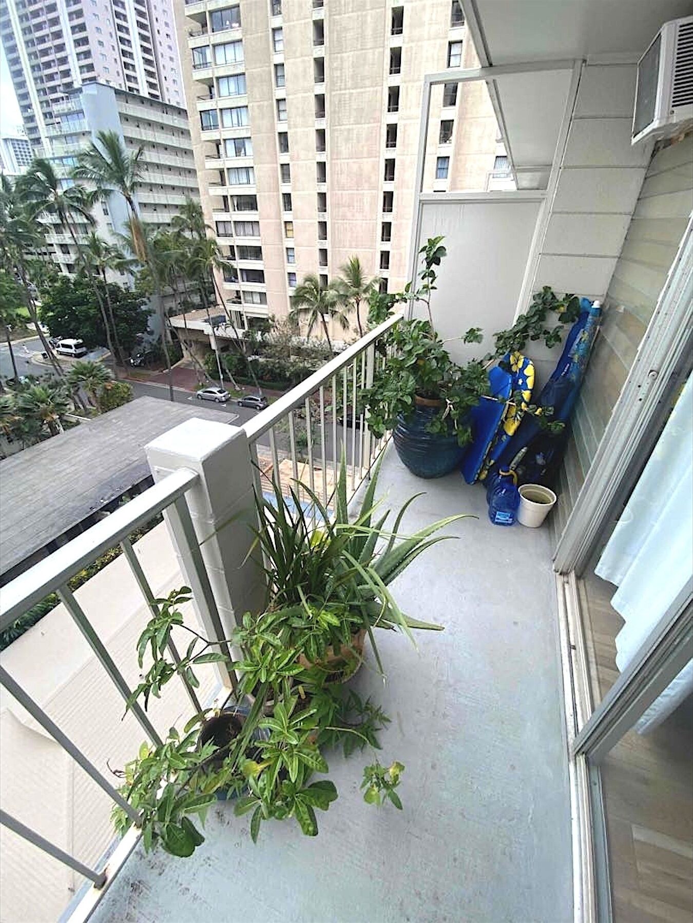 Ein Balkon mit Blumentöpfen, Blick auf eine Stadtlandschaft und ein mehrstöckiges Gebäude.