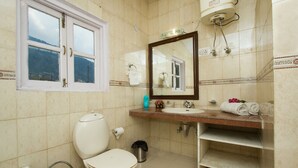 A bathroom with a toilet, sink, mirror, and window.