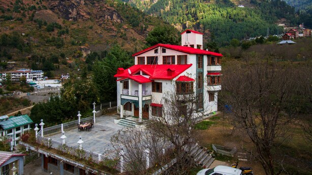 A multi-story building with a red roof, situated on a hillside with a mountainous backdrop.