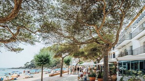 Un paseo marítimo con árboles, sombrillas de playa y gente.