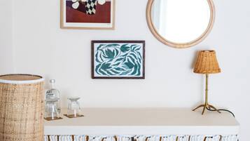 A white console table with a mirror, framed artwork, a wicker lamp, and a decorative vase.