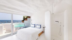 Un dormitorio moderno con una cama grande, un balcón con cerramiento de vidrio y una ducha a ras de suelo.