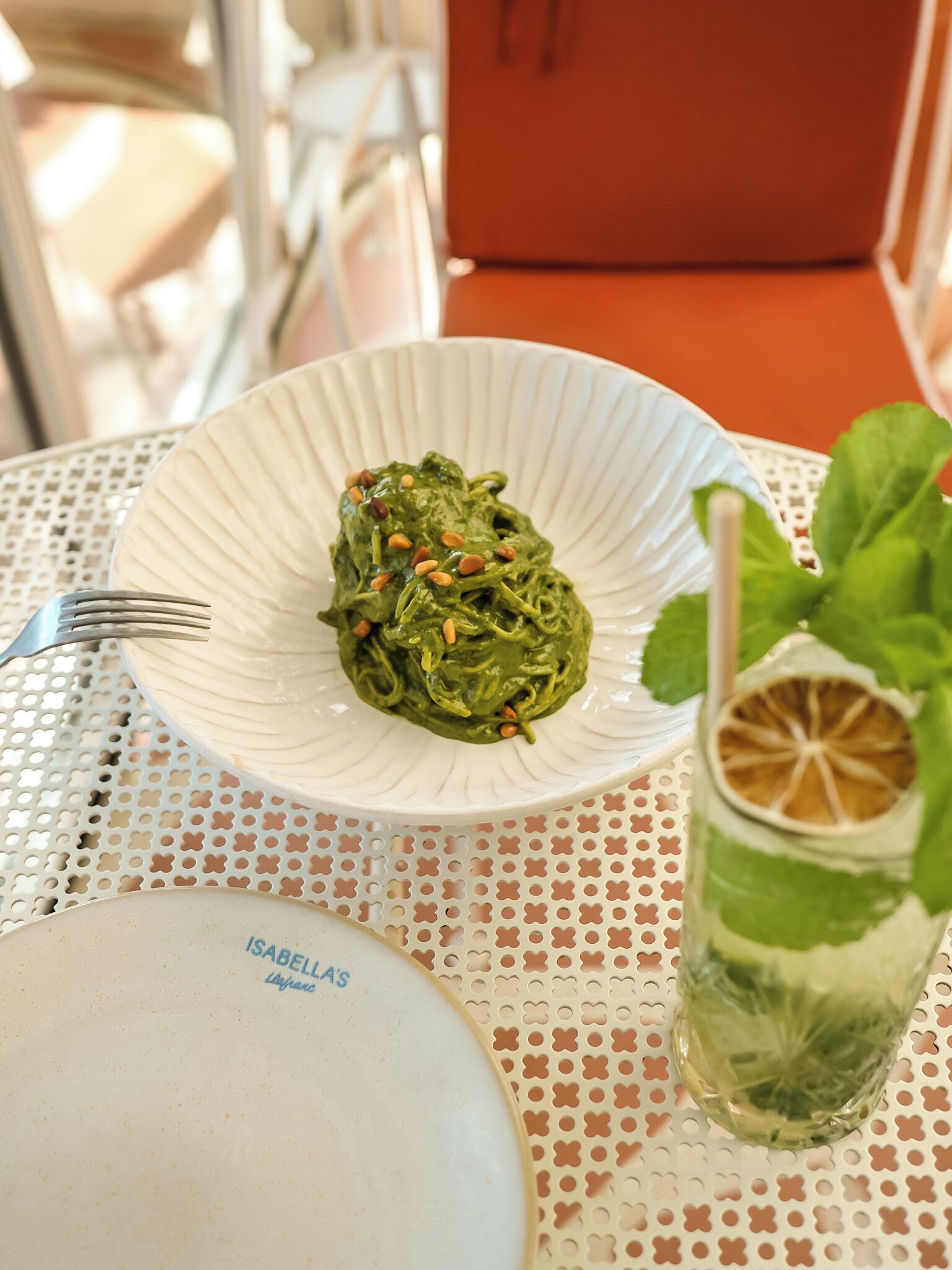 A table with a plate of pasta, a glass of drink, and a fork.