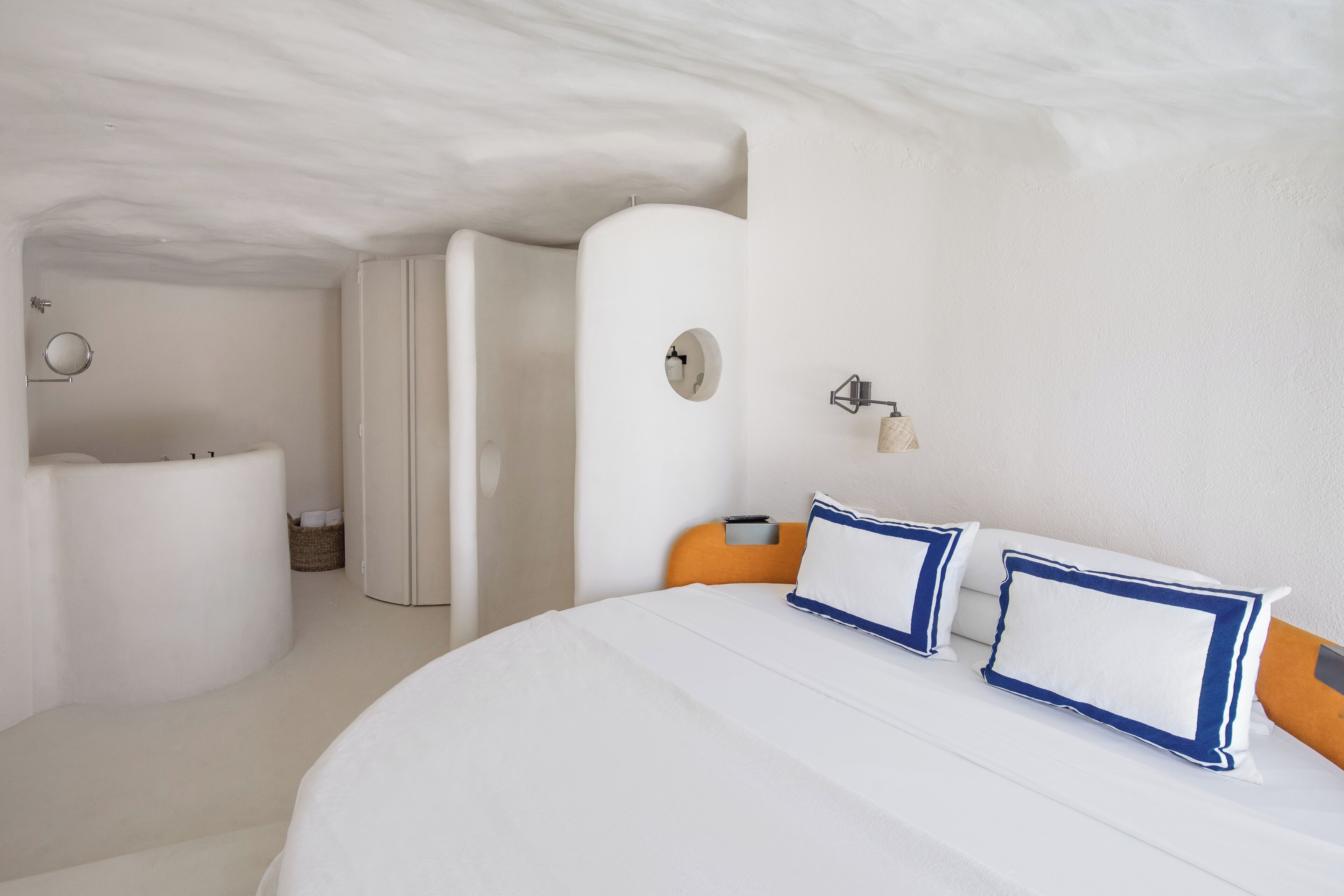 Een slaapkamer met een groot bed, een nachtkastje, een klok aan de muur, en een badkamer met een bad en toilet.