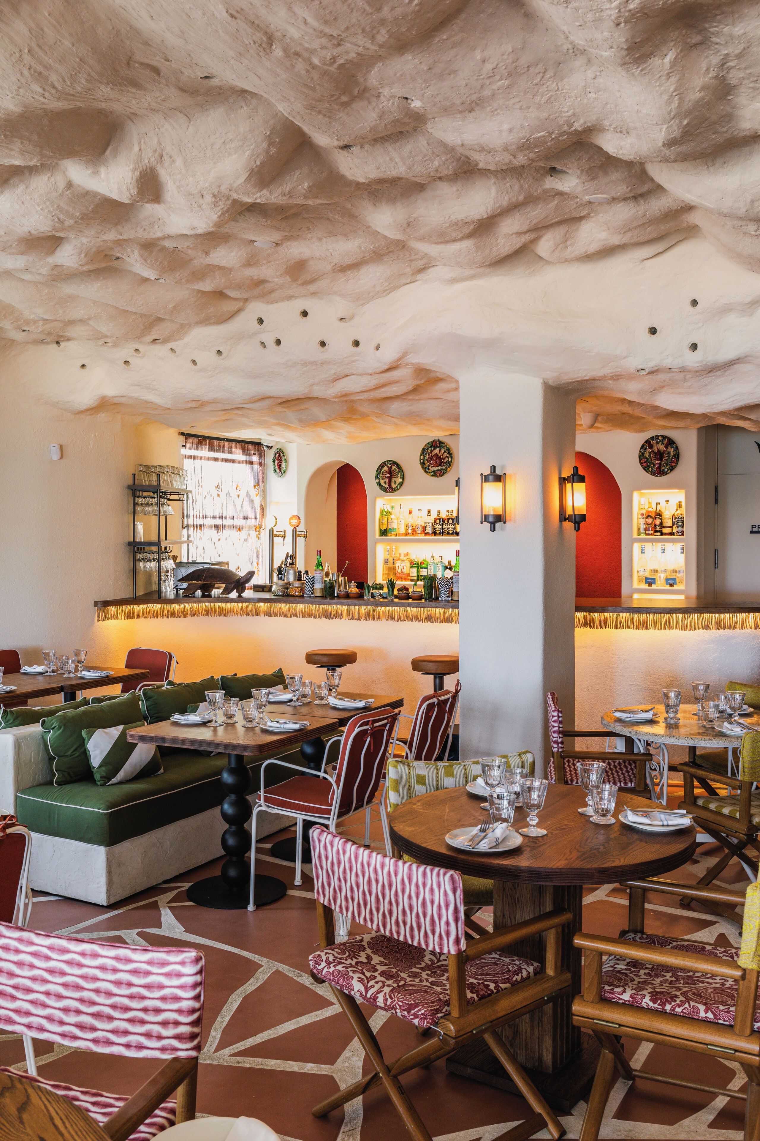 A restaurant with a bar area, seating arrangements, and a unique ceiling design.