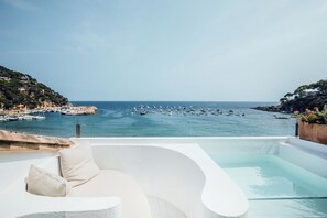 Ein moderner Infinity-Pool mit weißem Infinity-Rand, mit Blick auf eine Marina mit Booten und eine Küstenlandschaft.