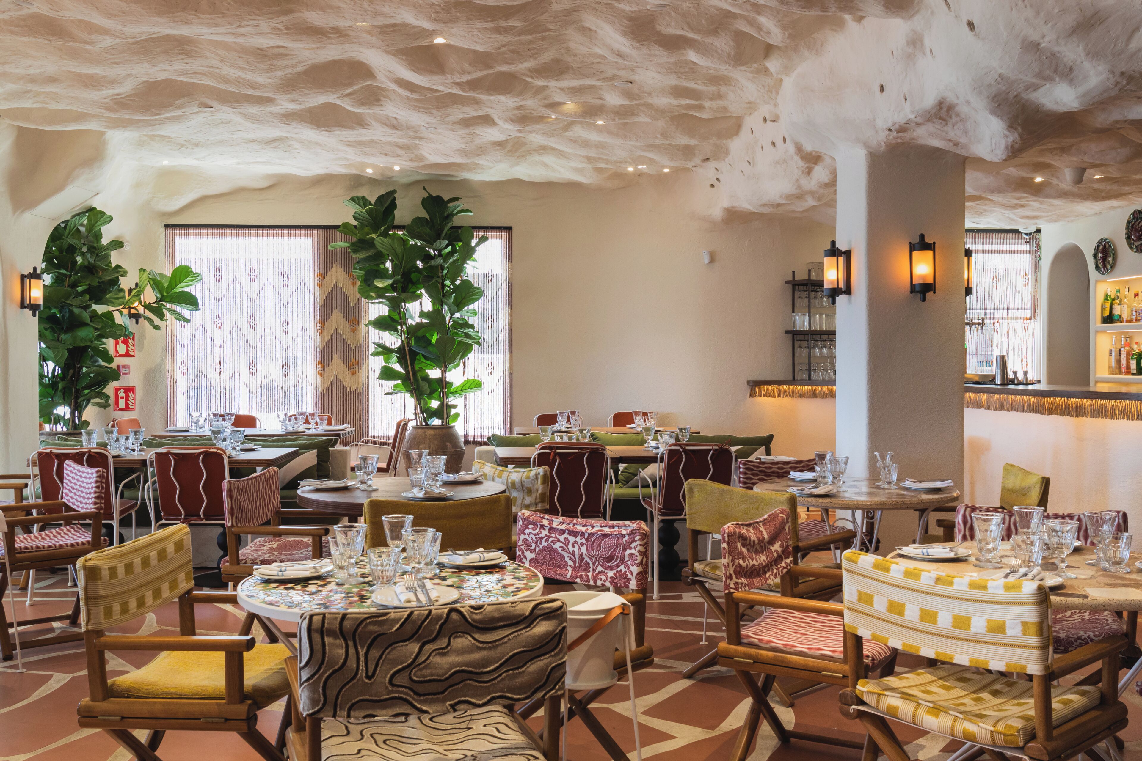 Un restaurant avec des tables rondes, des chaises rembourrées et un plafond à la texture unique.