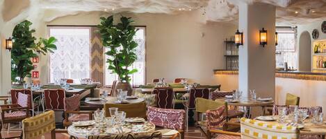 A restaurant with round tables, cushioned chairs, and a ceiling with a unique texture.