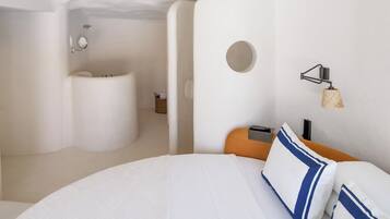 Habitación de hotel moderna con una cama grande, un espejo redondo, un baño pequeño y una lámpara fijada a la pared.