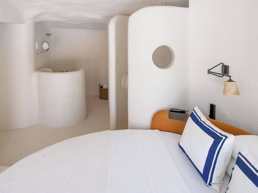 Habitación de hotel moderna con una cama grande, un espejo redondo, un baño pequeño y una lámpara fijada a la pared.