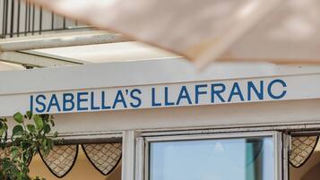 A sign reading "ISABELLA'S LLAFRANC" above a doorway with a view of the sea.