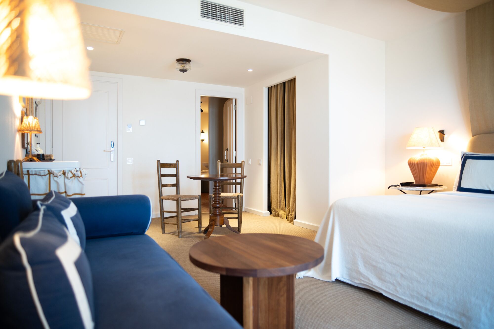 Una habitación de hotel con una cama, un sofá azul, una mesa de comedor de madera con sillas y una pequeña mesa redonda.