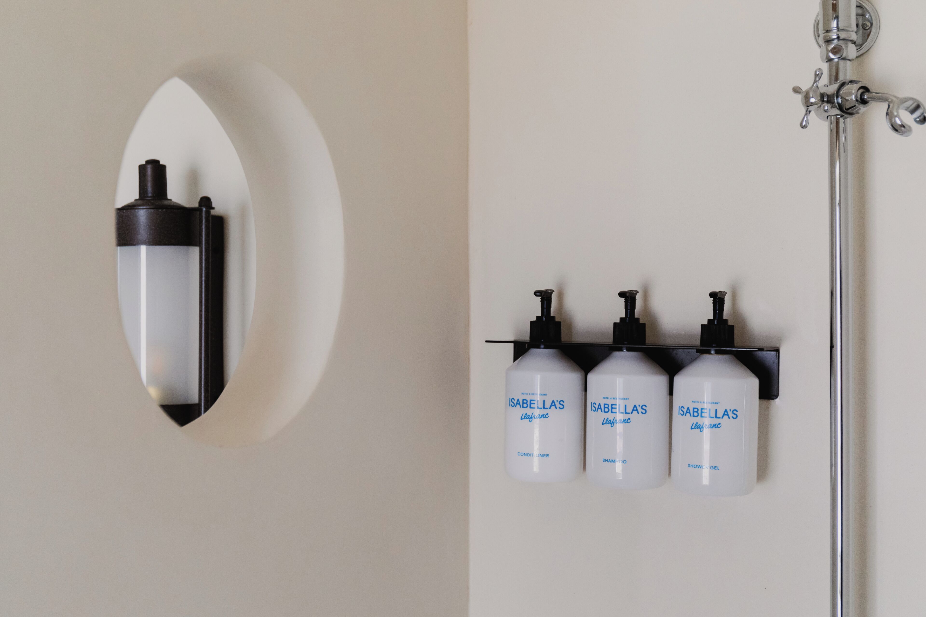 A bathroom with a wall-mounted light fixture and three bottles of Isabella's products.