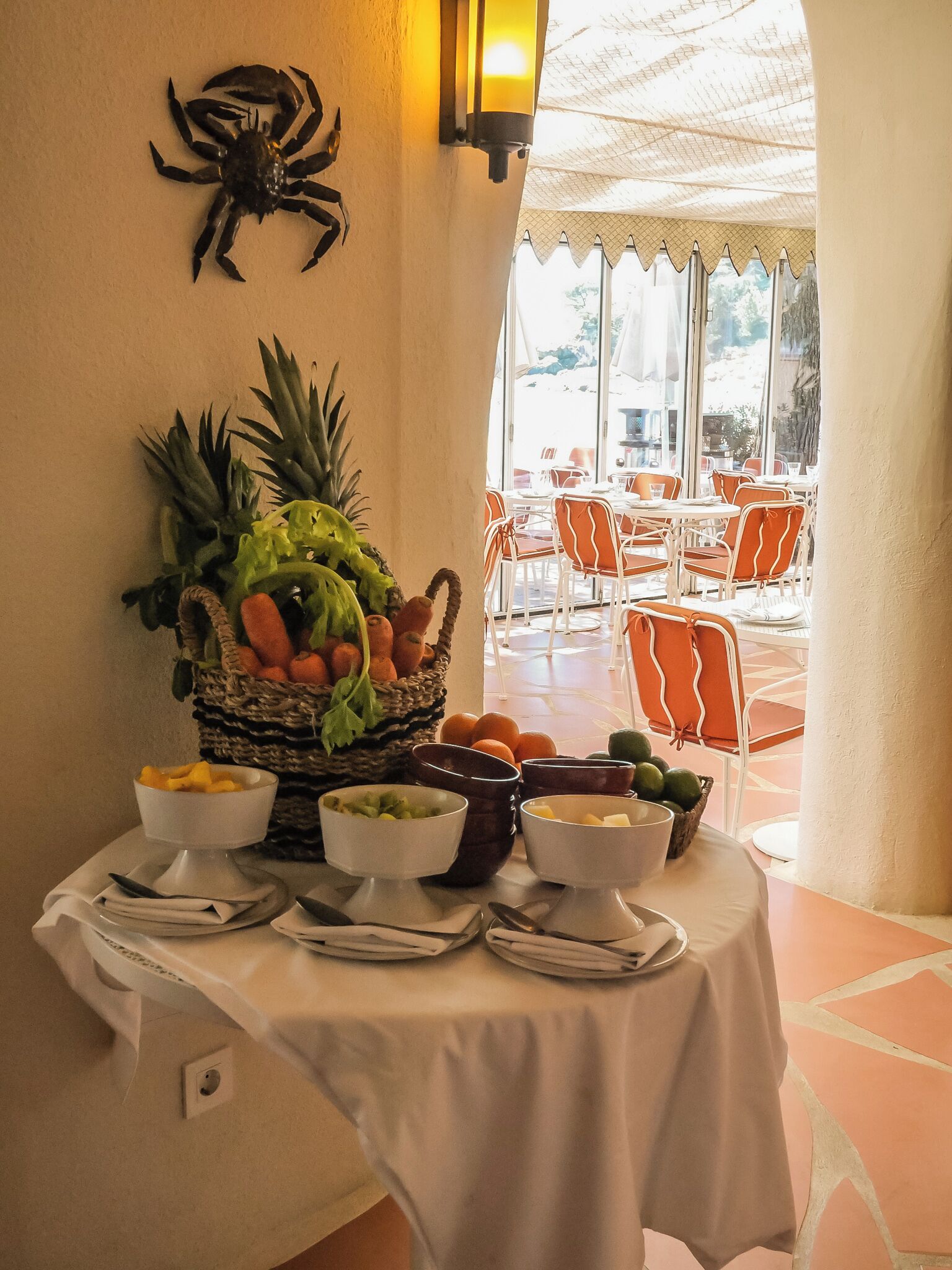 A table with fruit bowls and a decorative basket, a wall-mounted spider decoration, and a view of outdoor seating area.